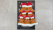 Family ornament with 7 brown gingerbread figures in red Christmas hats, shown on backing card and Christmas tree.