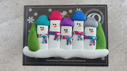 Family ornament with 5 snowmen in colourful scarves, hemmed by Christmas trees, shown on backing card and Christmas tree.