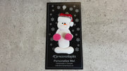 Ornament of white snowman in red hat holding pink cheerleader pom-poms, shown on backing card and Christmas tree.