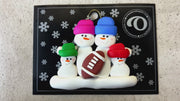 Family ornament with 4 white snowmen in bright hats with a football, shown on backing card and Christmas tree.