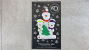 Family ornament with 1 large and 2 small white snowmen in bright scarves, with green Christmas tree, shown on backing card and Christmas tree.