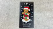 Tan bear in red festive hat holding colourful present ornament, shown on backing card and Christmas tree.