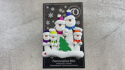 Family ornament with 5 white snowmen in bright scarves, with green Christmas tree, shown on backing card and Christmas tree.