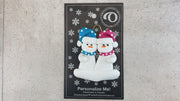 A couple’s ornament of two white snowmen in polka dot scarves and hats, shown on backing card and Christmas tree.