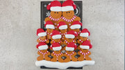 Family ornament with 13 brown gingerbread figures in red Christmas hats, shown on backing card and Christmas tree.