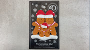 Family ornament with 3 brown gingerbread figures in red Christmas hats, shown on backing card and Christmas tree.