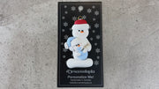 Family ornament with 1 large and 1 infant snowman in blue, shown on backing card and Christmas tree.