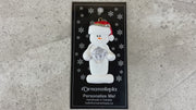 Ornament of white snowman in red hat holding large plastic diamond, shown on backing card and Christmas tree.