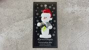 Ornament of white snowman in red hat holding a pair of scissors and various scrapbooking papers, shown on backing card and Christmas tree.
