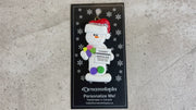 Ornament of white snowman in red hat holding various medications and a medical chart, shown on backing card and Christmas tree.