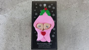 Ornament with twin infant heads poking out of a pink baby blanket, shown on backing card and Christmas tree.