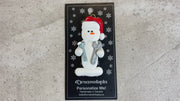 Ornament of white snowman in red hat holding a wrench and a screw, shown on backing card and Christmas tree.