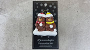 A couple’s ornament of two brown bears in polka dot scarves and hats, shown on backing card and Christmas tree.