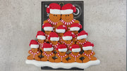 Family ornament with 14 brown gingerbread figures in red Christmas hats, shown on backing card and Christmas tree.
