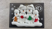 Family ornament with 2 large and 2 small snowmen in hats, holding holiday objects, shown on backing card and Christmas tree.