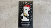 Ornament of white snowman in red hat holding a fancy shoe, shown on backing card and Christmas tree.