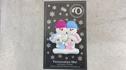 Family ornament with 2 large and 2 infant snowmen in pink and blue, shown on backing card and Christmas tree.