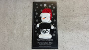 Ornament of white snowman in red hat holding black laptop and a computer mouse, shown on backing card and Christmas tree.