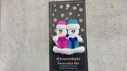 Family ornament with 2 white snowmen in colourful hats holding matching presents, shown on backing card and Christmas tree.