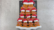 Family ornament with 12 brown gingerbread figures in red Christmas hats, shown on backing card and Christmas tree.