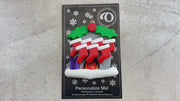 Vibrant fireplace ornament with holly and presents, displaying 7 red stockings, shown on backing card and Christmas tree.