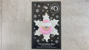 Baby ornament with infant face and pink hat on glittery white snowflake base, shown on backing card and Christmas tree.