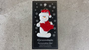 White snowman with red festive hat and maple leaf ornament, shown on backing card and Christmas tree.