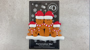 Family ornament with 4 brown gingerbread figures in red Christmas hats, shown on backing card and Christmas tree.