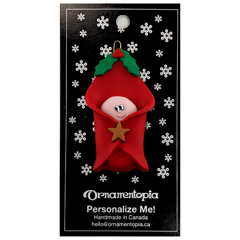 Ornament with an infant head poking out of a red baby blanket, on display backing card.