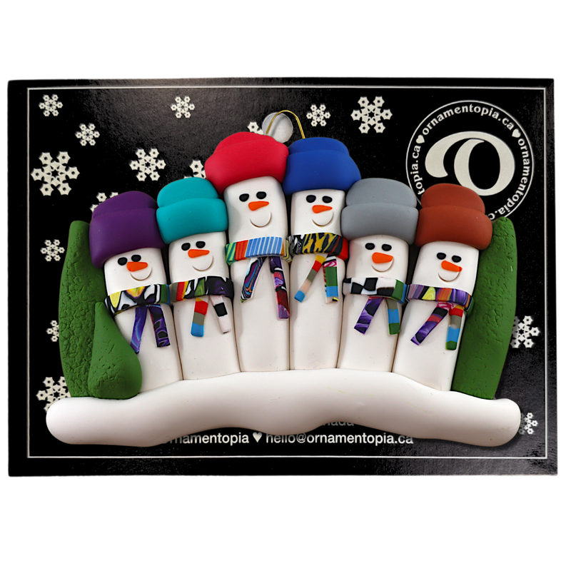 Family ornament with 6 snowmen in colourful scarves and hats, hemmed by Christmas trees, on display backing card.