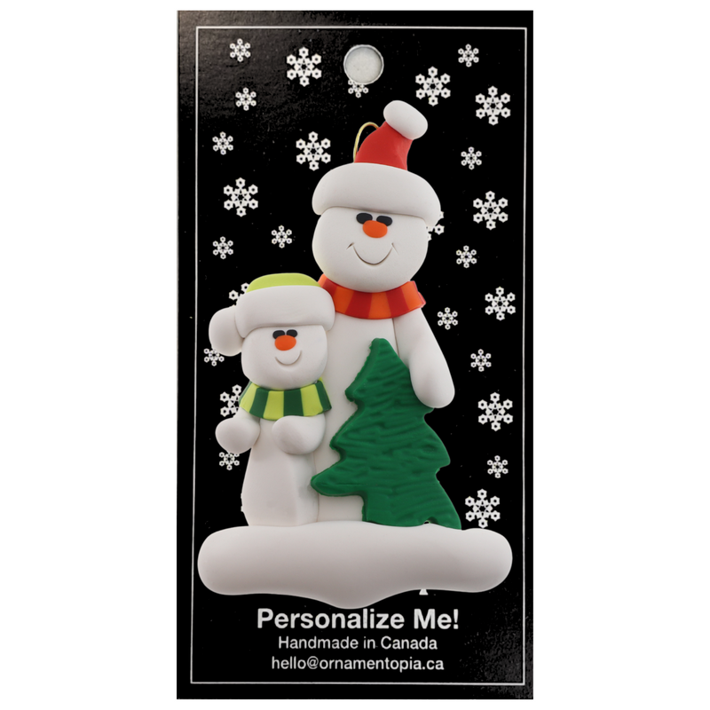 Family ornament with 1 large and 1 small white snowman in bright scarves, with green Christmas tree, on display backing card.