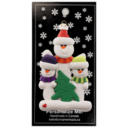 Family ornament with 1 large and 2 small white snowmen in bright scarves, with green Christmas tree, on display backing card.