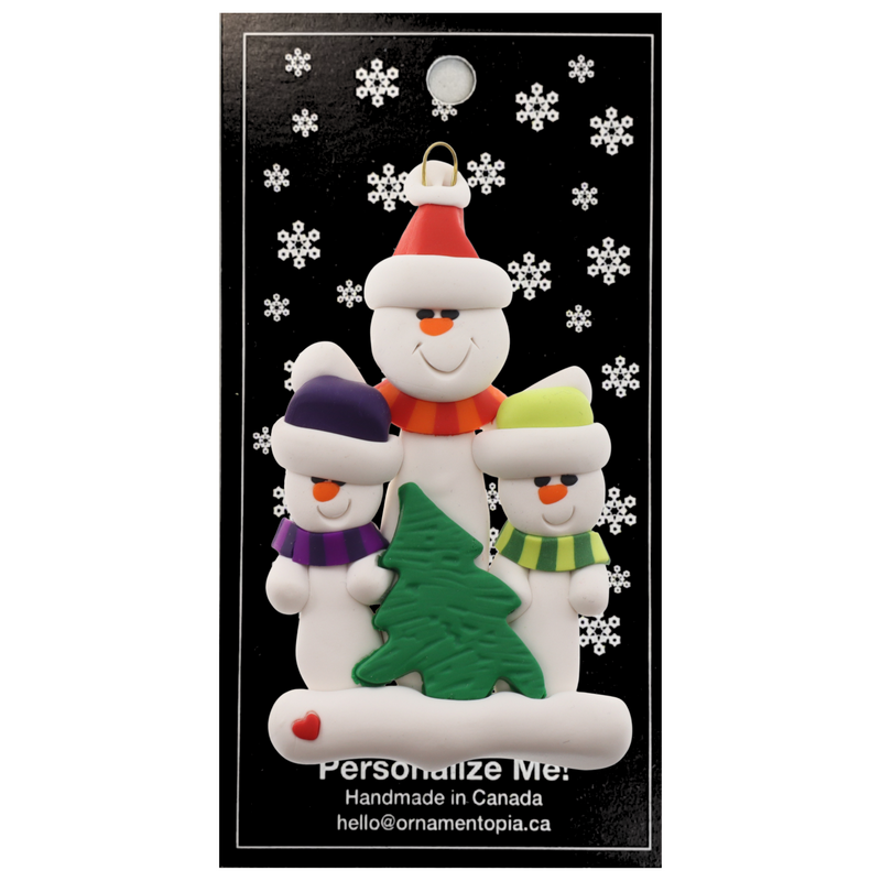 Family ornament with 1 large and 2 small white snowmen in bright scarves, with green Christmas tree, on display backing card.