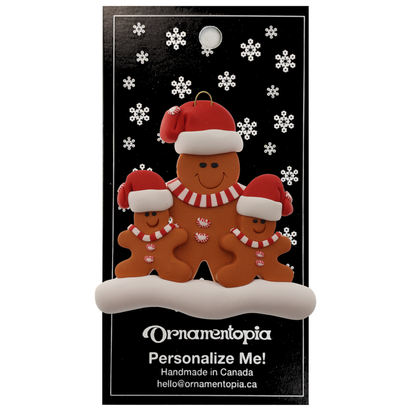 Family ornament with 1 large and 2 small brown gingerbread figures in red Christmas hats, on display backing card.