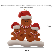 Family ornament with 1 large and 2 small brown gingerbread figures in red Christmas hats, graphed to show size (6x7cm).