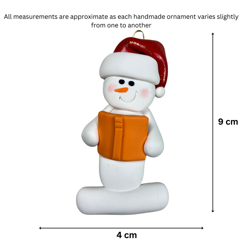 Ornament of white snowman in red hat holding an orange book, graphed to show size (4x9cm).