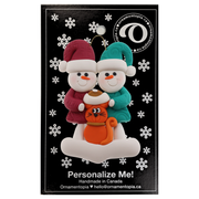 Ornament of snowman couple in red and green shirts and hats with a orange cat in Christmas hat, on a display backing card.