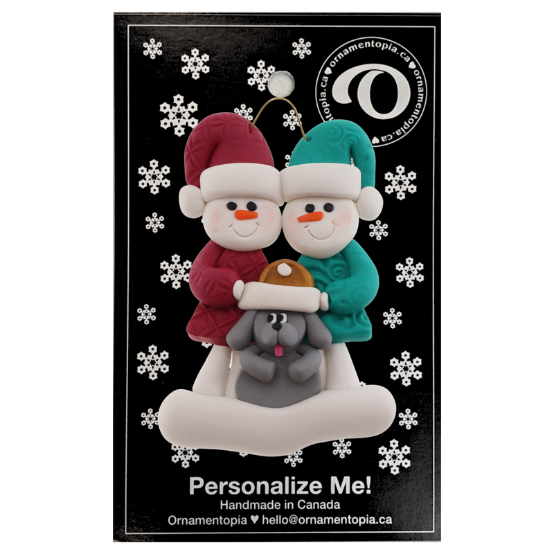 Ornament of snowman couple in red and green shirts and hats with grey dog in Christmas hat, on display backing card.