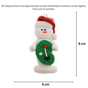 Ornament of white snowman in red hat holding a mini grass green with a golf ball and a flagstick, graphed to show size (4x9cm).