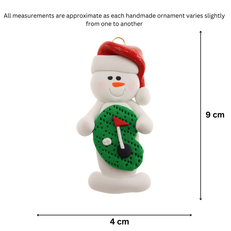 Ornament of white snowman in red hat holding a mini grass green with a golf ball and a flagstick, graphed to show size (4x9cm).