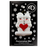 A couple’s ornament of two white snowmen holding a red heart together, on display backing card.