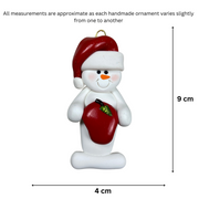 Ornament of white snowman in red hat holding a shiny red apple, graphed to show size (4x9cm).