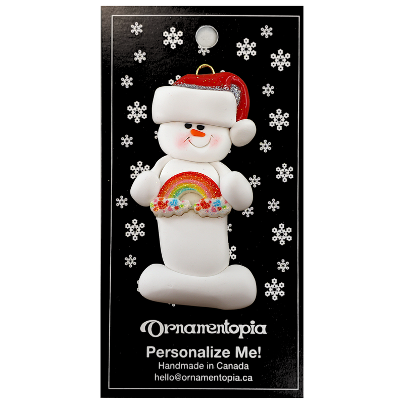 White snowman with small rainbow and red festive hat ornament, on display backing card.