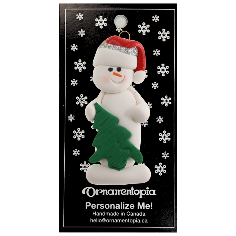 White snowman in red festive hat with green Christmas tree ornament, on display backing card.