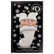 Ornament with twin infant heads in white glitter hats poking out of a white glitter stocking, on display backing card.