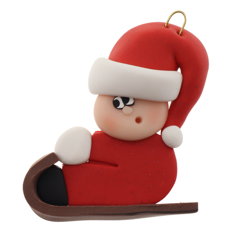 Small figure in red outfit and festive hat riding on brown toboggan ornament.