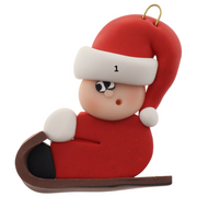 Small figure in red outfit and festive hat riding on brown toboggan ornament, numbered for personalization.