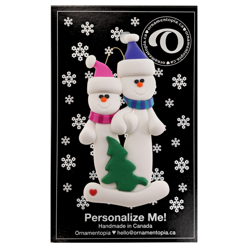 Family ornament with 2 white snowmen in bright scarves, with green Christmas tree, on display card backing.