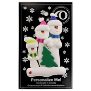 Family ornament with 3 white snowmen in bright scarves, with green Christmas tree, on display card backing.