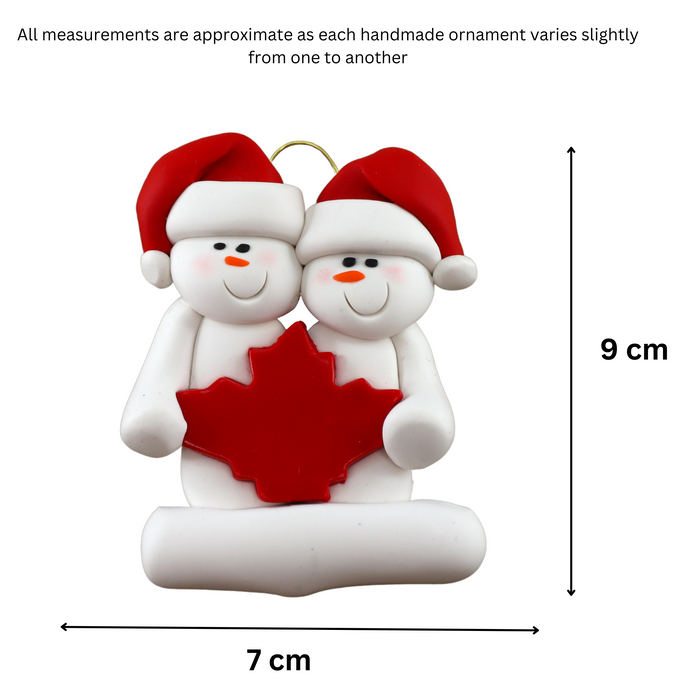 Family ornament with 2 white snowmen in red hats, gathered around a red maple leaf, graphed to show size (7x9cm).